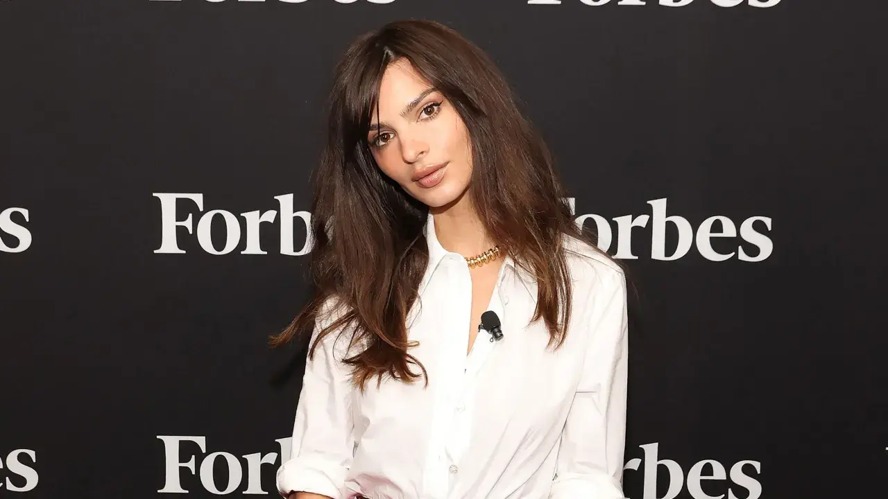 Emily Ratajkowski mit langen, gestuften Haaren und einem weißen Hemd vor einem Forbes-Banner.