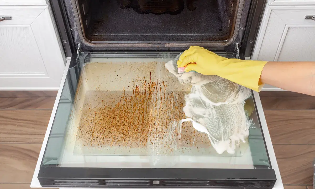 Gelbe Handschuhe reinigen mit Schaum die stark verschmutzte Backofentür.