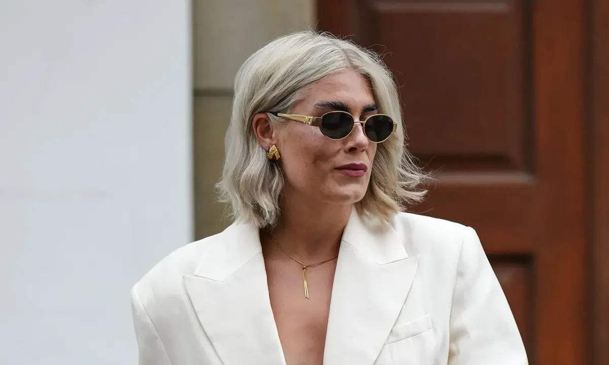 Moderne Frau mit gestuften Frisuren ab 50 mit Brille, trägt cremefarbenen Blazer und auffälligen Schmuck.