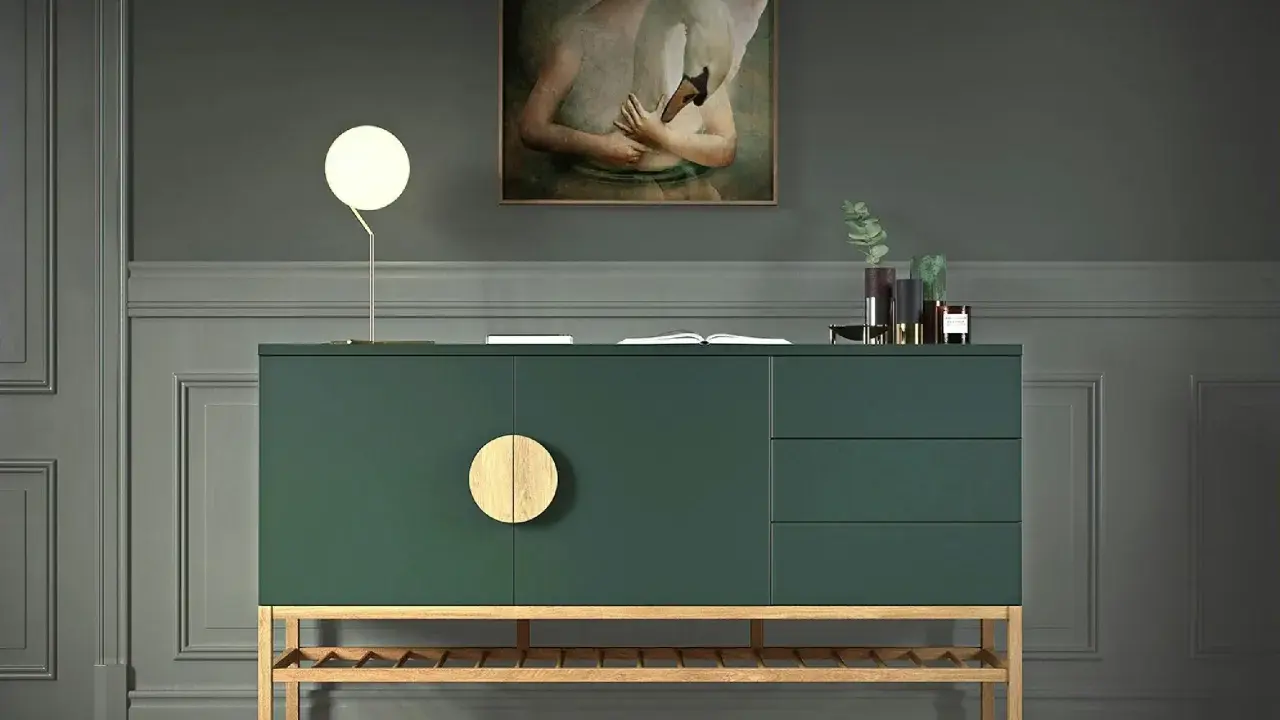 Ein grünes Sideboard mit Holzdetails, dekoriert mit einer Lampe, einem Buch und Vasen. Ein Gemälde mit einem Schwan hängt darüber.