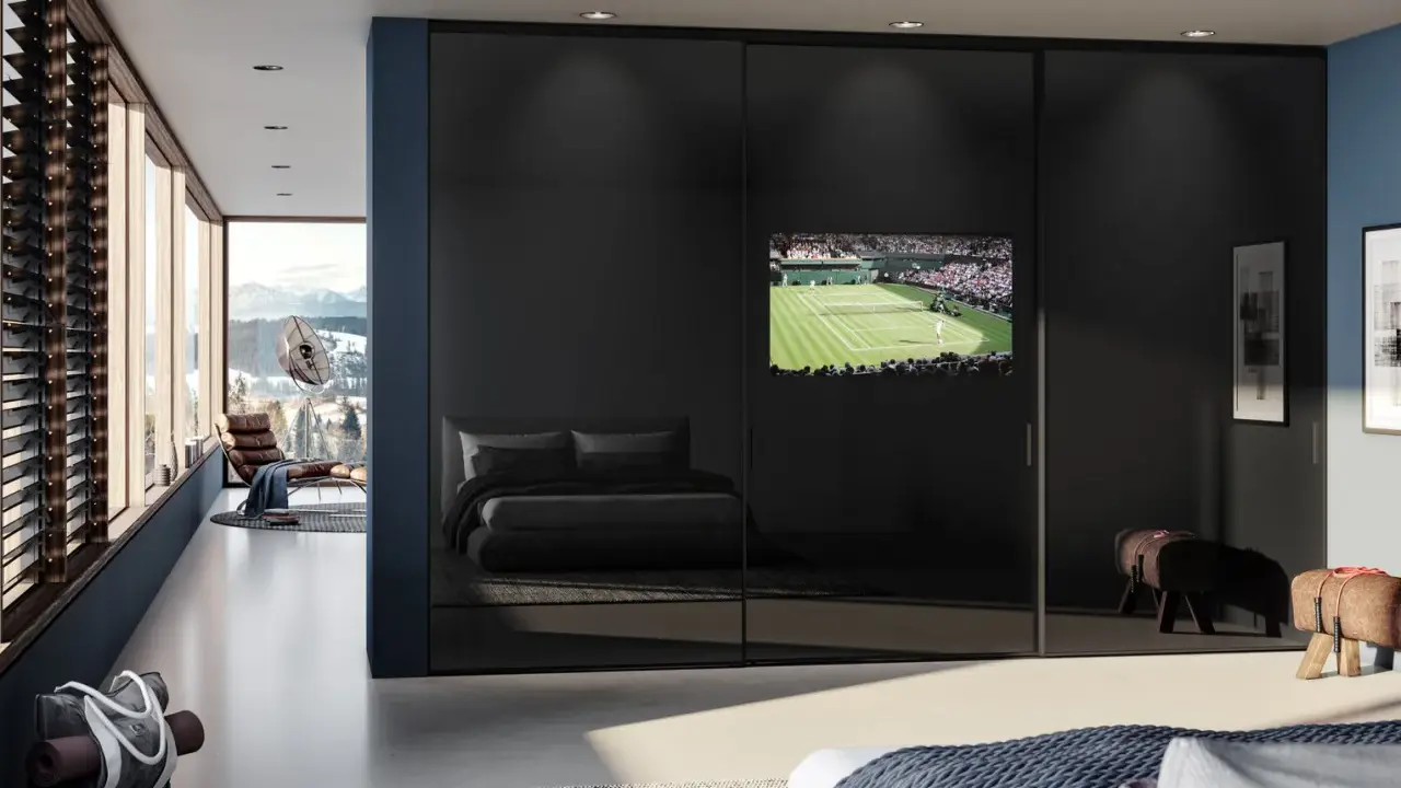 Ein moderner Kleiderschrank mit Spiegeltüren beherbergt einen integrierten Fernseher im Schlafzimmer, der ein Tennismatch zeigt.