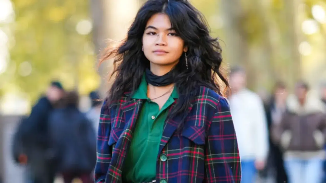 Junge Frau mit voluminösem, flauschigem Haar, trägt karierten Blazer und grünes Poloshirt.