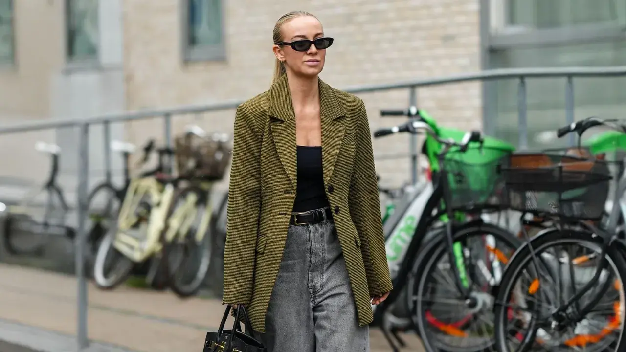 Stilvolle Frau mit Sonnenbrille und kariertem Blazer, die zeigt, wie man graue Jeans kombiniert.