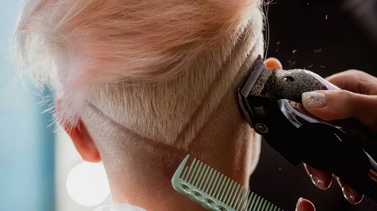 Eine Frau bekommt einen modernen Undercut. Haare werden mit einem Trimmer geschnitten, ein Kamm hält die Strähnen.