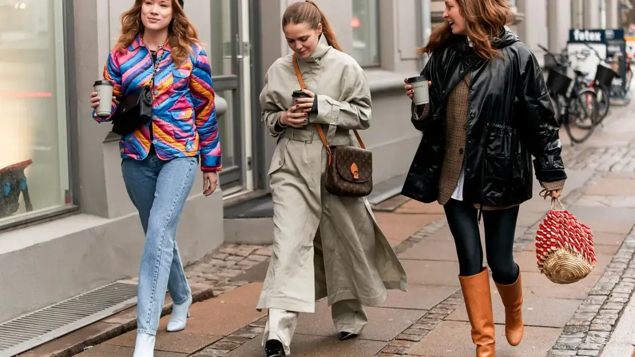 Drei Frauen spazieren mit Kaffee. Die mittlere trägt weite Hosen zu Pumps, die rechte Leggings zu Stiefeln. Die linke zeigt, welche Hose zu Boots Damen passt: Jeans zu weißen Stiefeletten.