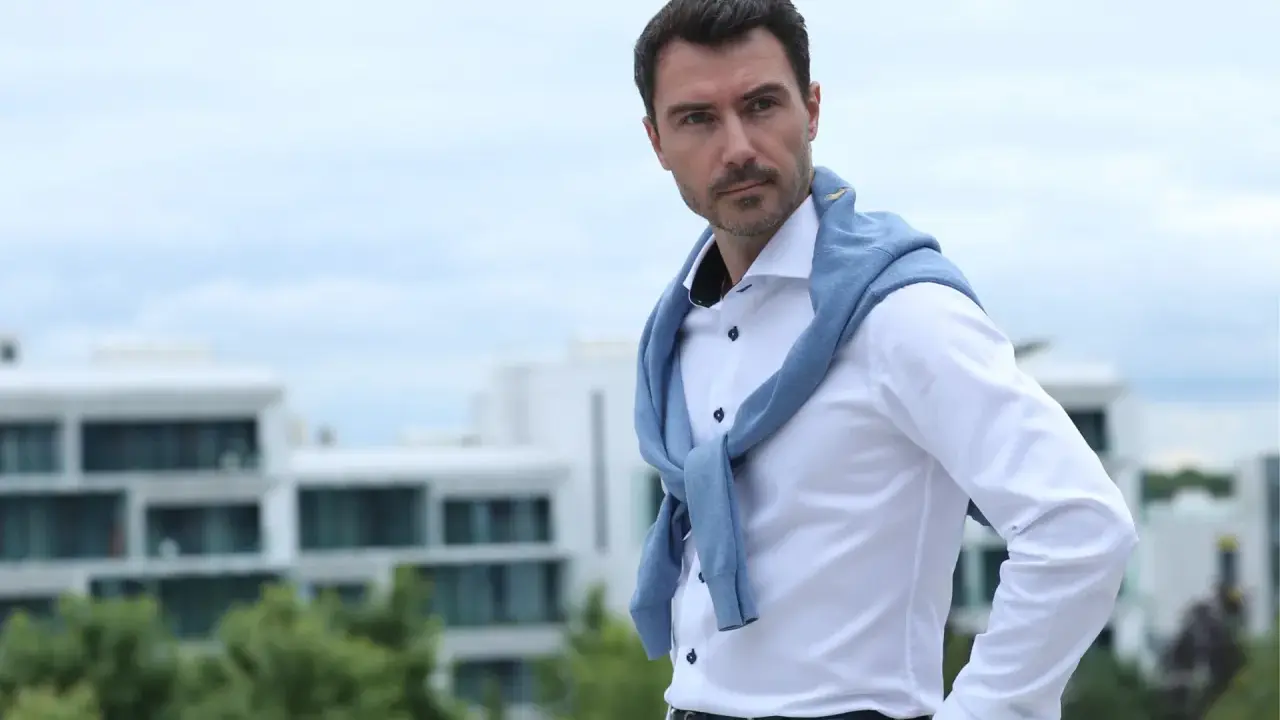 Mann mit klassischer old money hairstyle herren, trägt weißes Hemd und blauen Pullover über den Schultern.