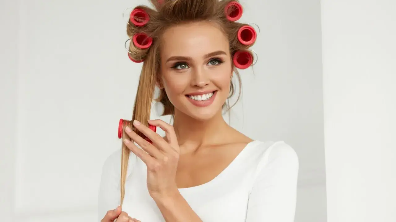 Lächelnde Frau mit roten Wicklern im Haar, die sich Locken macht.