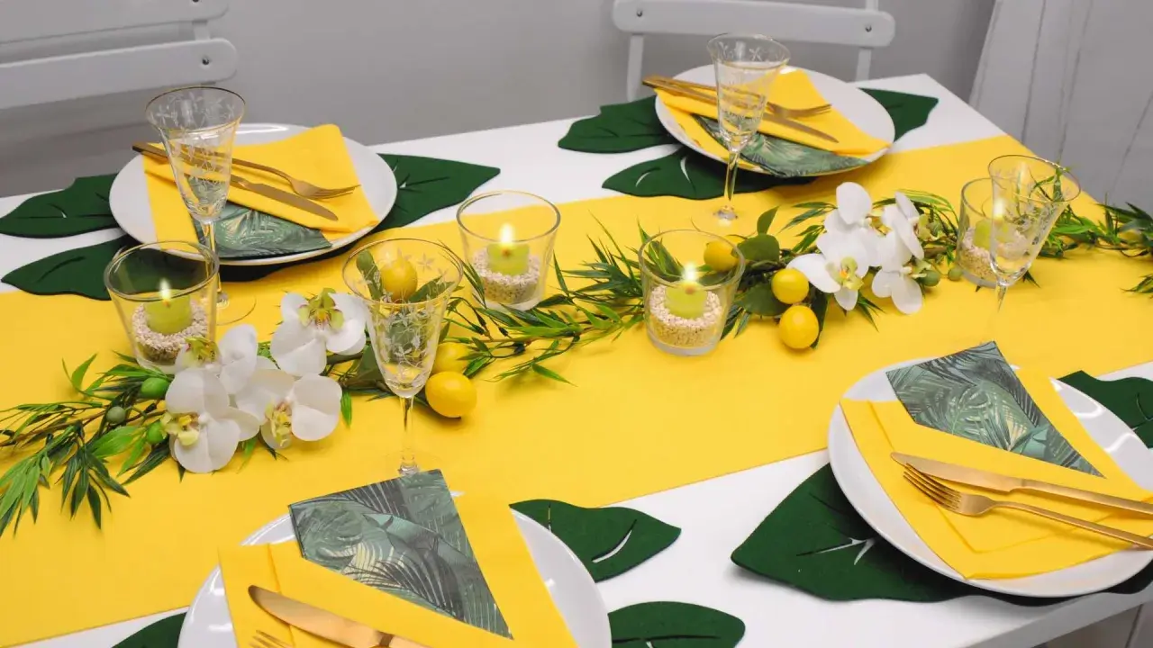 Sommerliche tischdeko mit zitronen, Orchideen und grünen Blättern. Kerzen in Gläsern sorgen für stimmungsvolles Licht.
