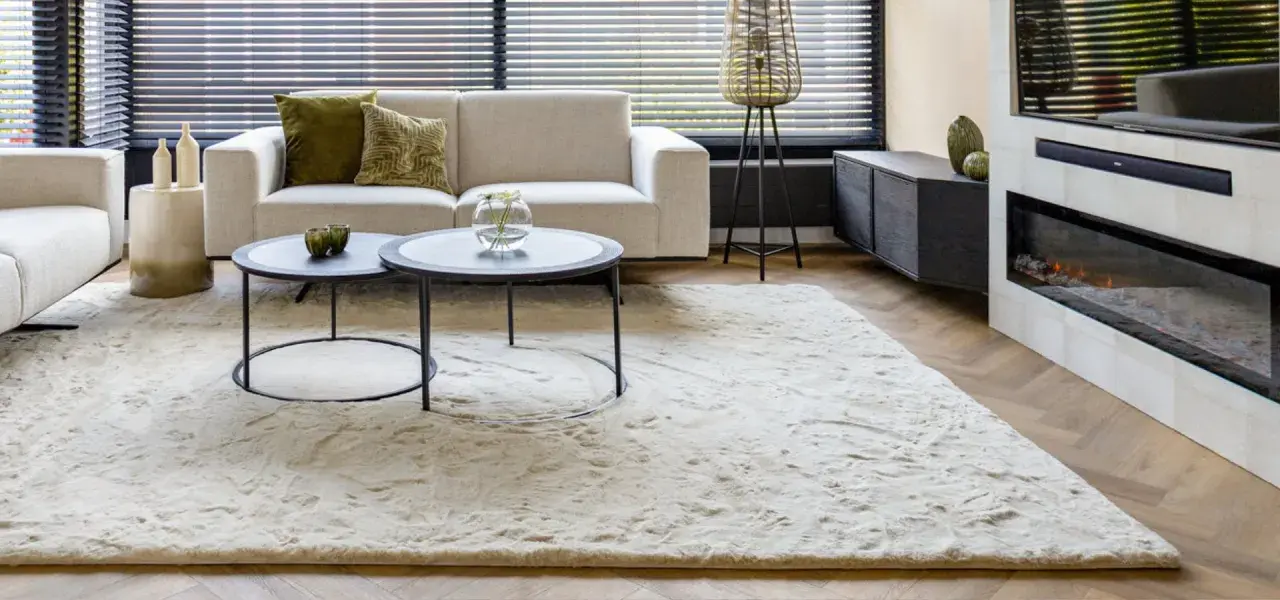 Ein heller, flauschiger Teppich liegt vor einem Sofa und einem Kamin. So wird der Teppich wieder flauschig gemacht.
