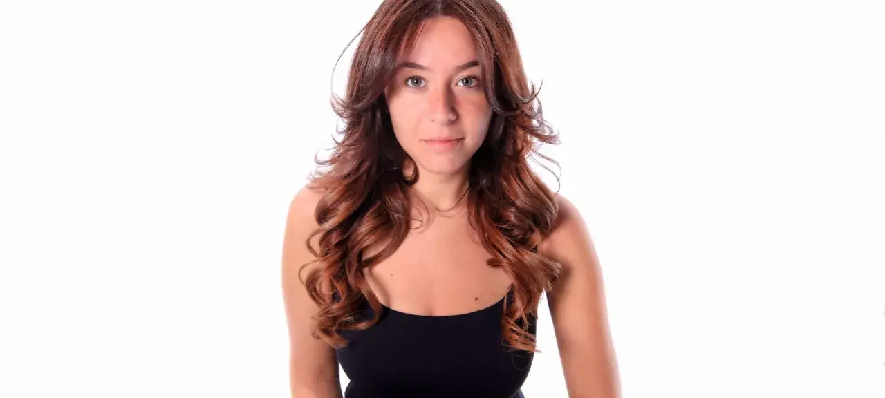 Frau mit langen, welligen Haaren im Butterfly Cut, die einen schwarzen Tanktop trägt.