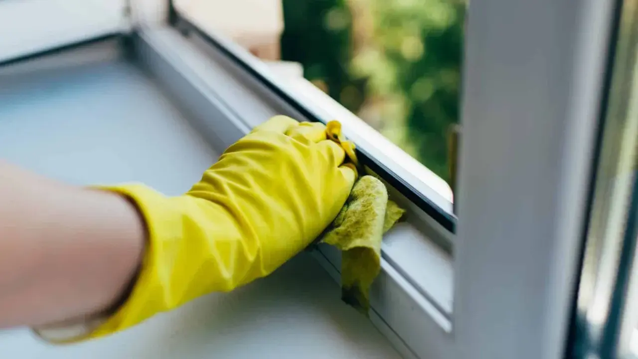 Gelbe Handschuhe reinigen den Kunststoff Fensterrahmen mit einem Tuch.