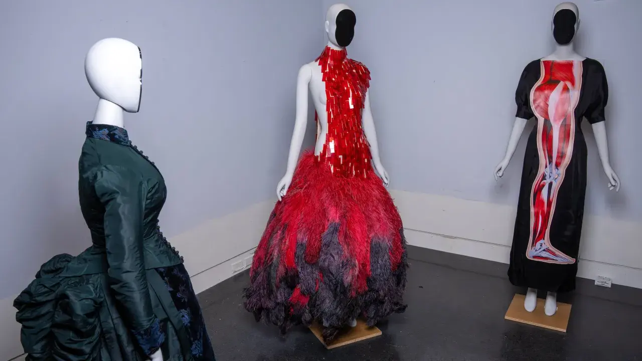Drei Schaufensterpuppen präsentieren extravagante Kleider, die an das Met Gala Thema erinnern: eines in Grün im viktorianischen Stil, eines in Rot mit Federn und eines mit anatomischem Druck.