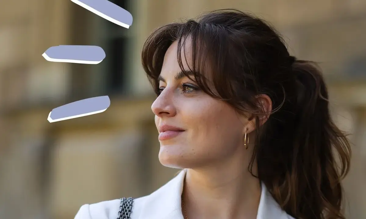 Frau mit rundem Gesicht und Curtain Bangs, trägt weißen Blazer.