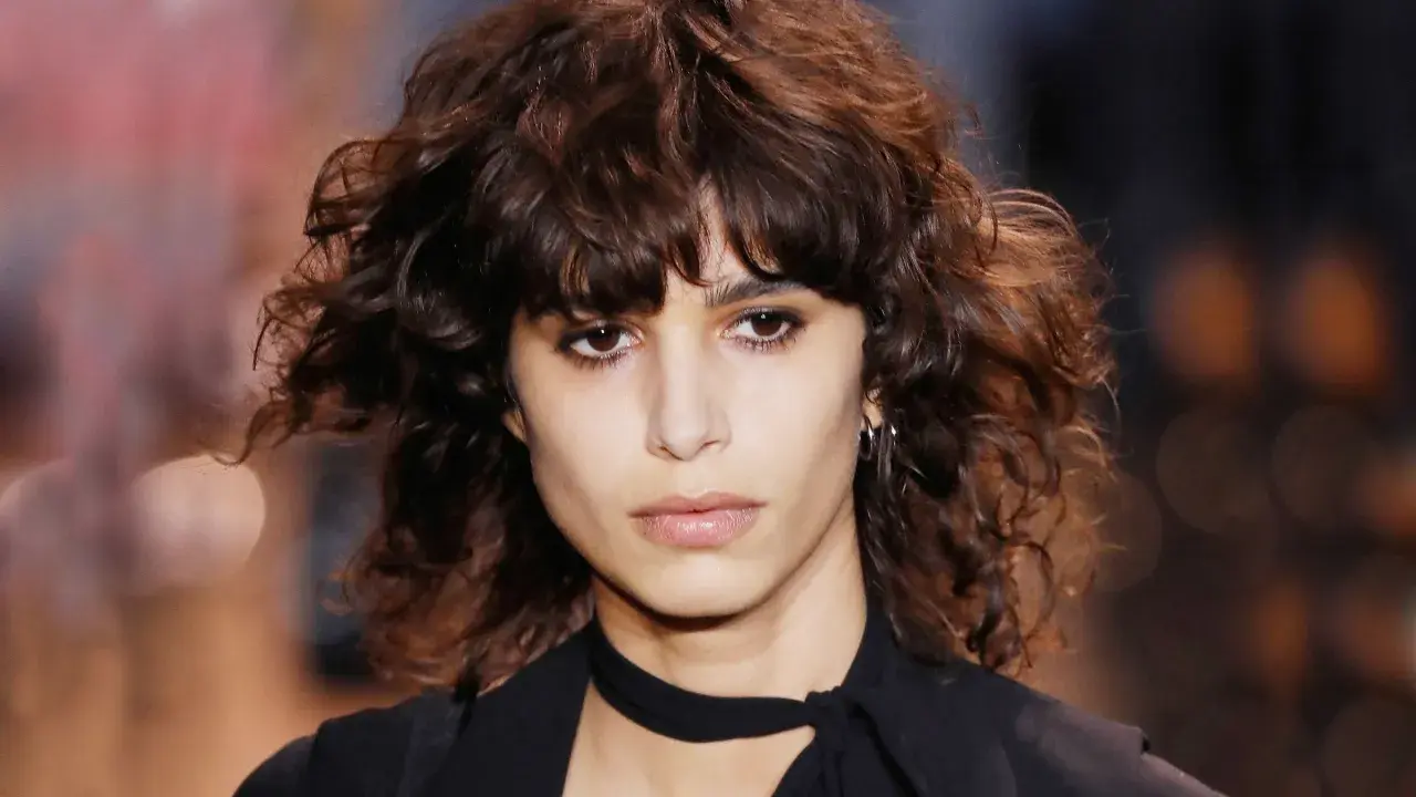 Ein Model mit einem lässigen shag cut und dunklen, welligen Haaren.