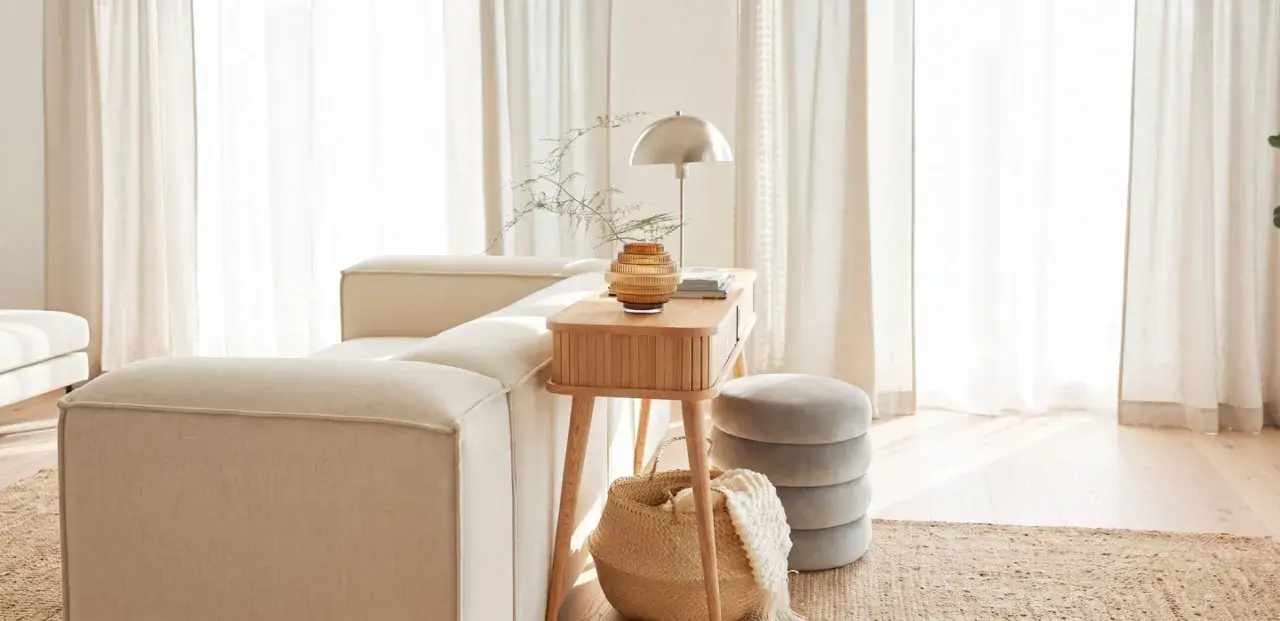 Gemütliches Wohnzimmer mit beigem Sofa, Holztisch, Lampe und Korb. Die helle Atmosphäre vermittelt das Gefühl von Hygge Bedeutung: Wohlbefinden und Gemütlichkeit.