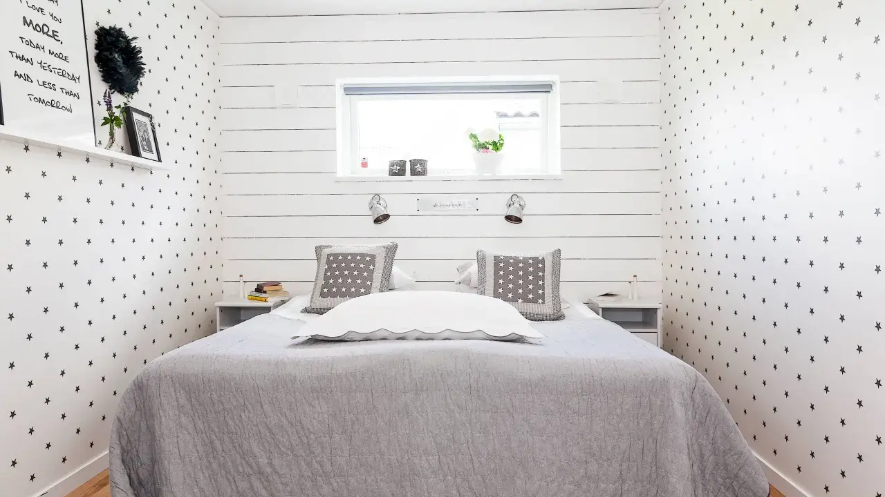 Gemütliches Schlafzimmer 10 qm einrichten: Sternen-Tapete, graue Decke, Nachttische und ein Bett mit Kissen.