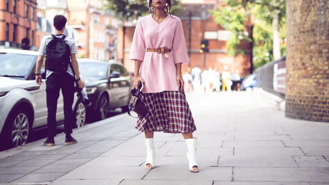 Ein Midirock kombiniert mit einem rosa Pullover und weißen Stiefeln – ein lässiger Sommer-Look auf der Straße.