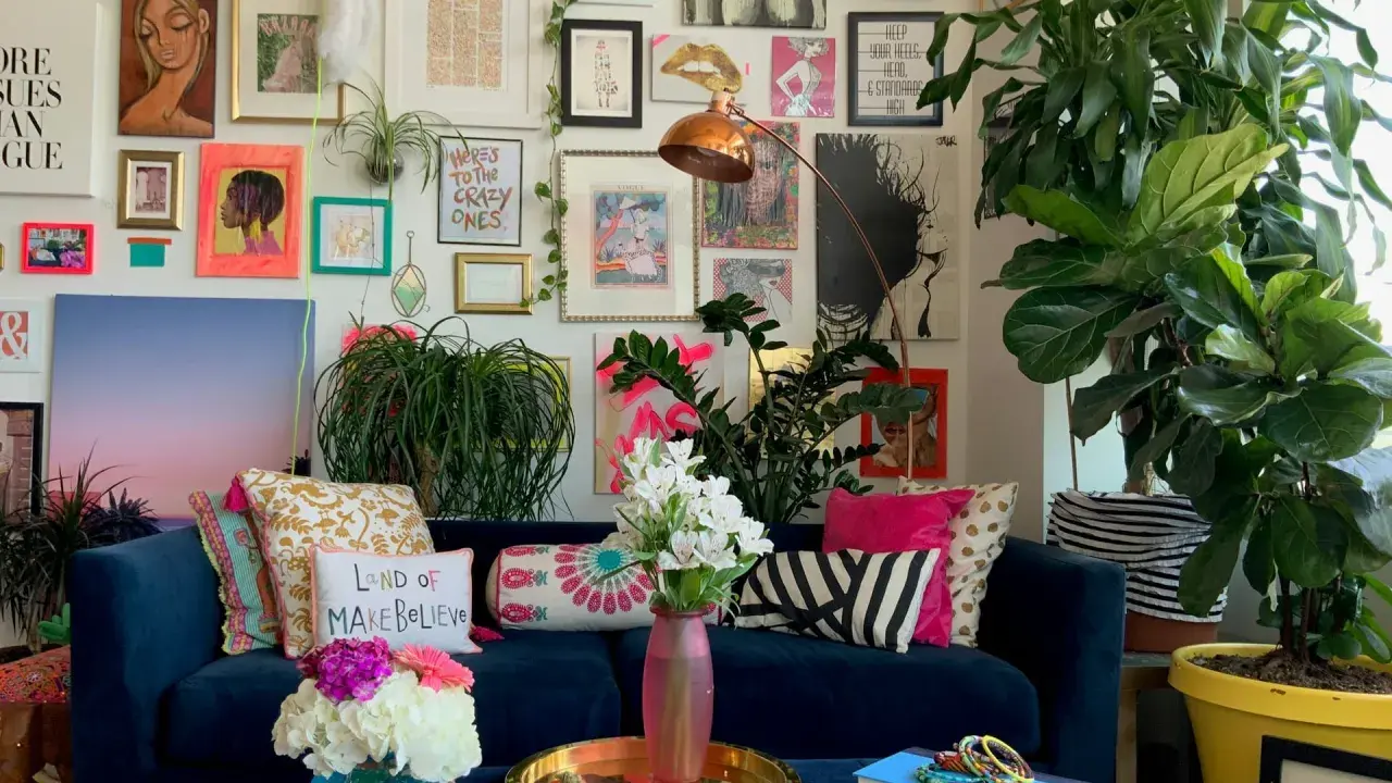 Ein Wohnzimmer im maximalistischen Stil mit einer blauen Couch, vielen Kissen, Pflanzen und einer Wand voller Kunstwerke und Drucke.