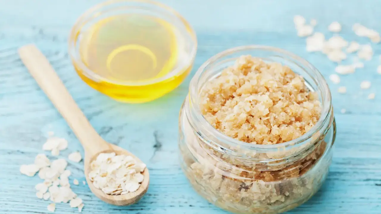 Zutaten für ein **Gesichtspeeling selber machen**: Haferflocken auf einem Holzlöffel, ein Glas mit Peeling und eine Schale mit Öl.
