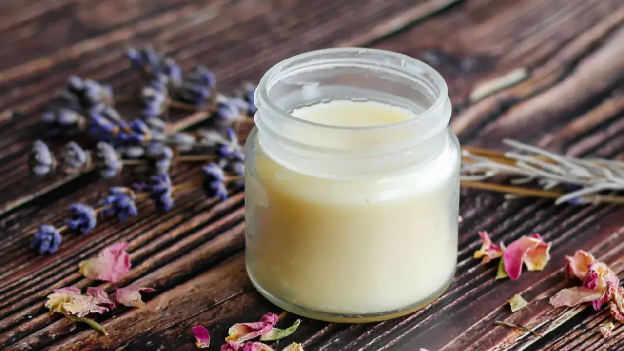 Ein Glas selbstgemachte Handcreme mit Lavendel und Rosenblüten auf Holzuntergrund.