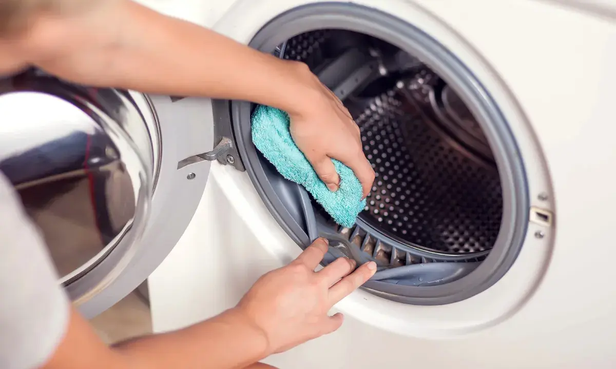 Hände reinigen die Gummidichtung der Waschmaschine mit einem blauen Tuch. Hausmittel helfen, die Waschmaschine zu reinigen und Gerüche zu vermeiden.