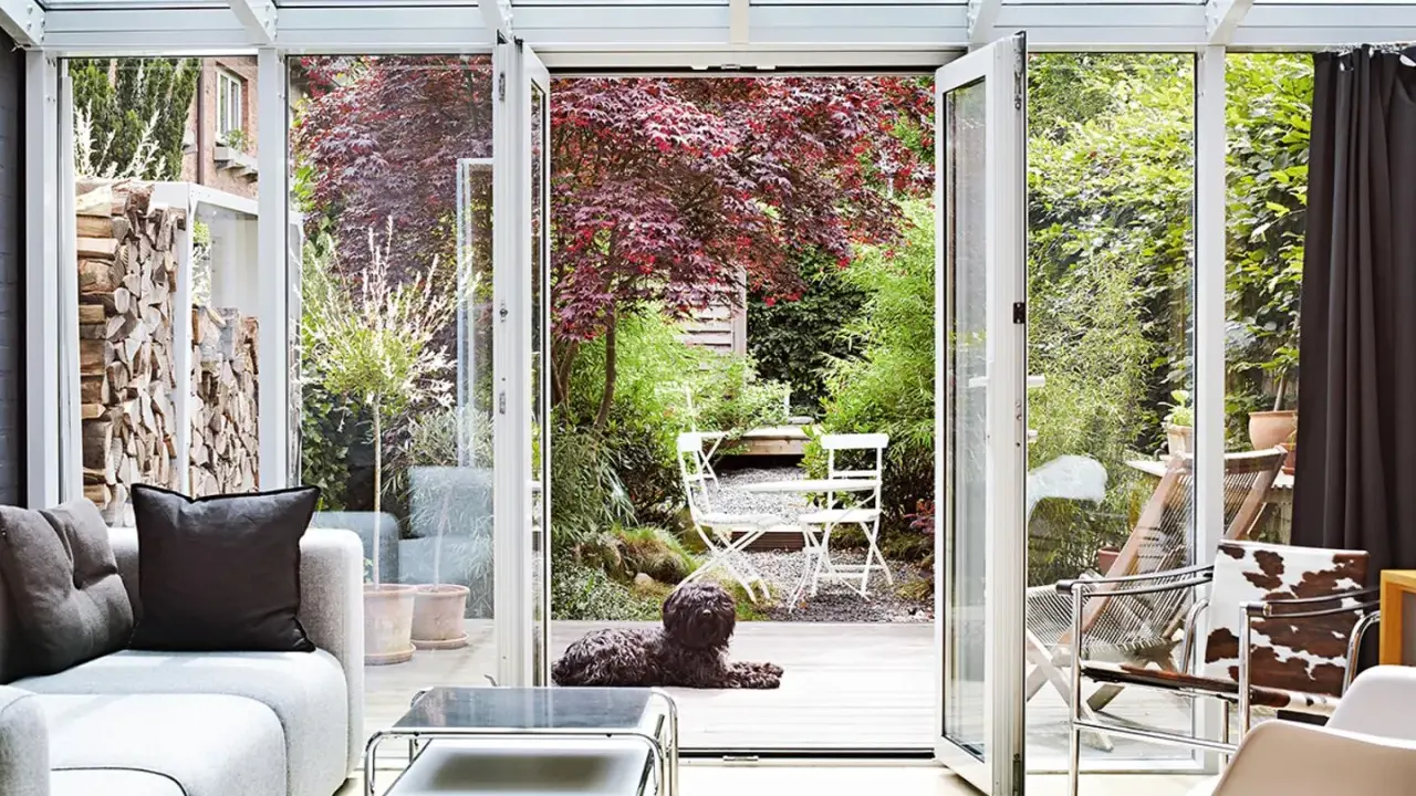 Gemütliche Wintergarten einrichten Ideen: Hund liegt auf Holzterrasse vor Garten mit rotem Ahornbaum und weißem Mobiliar.