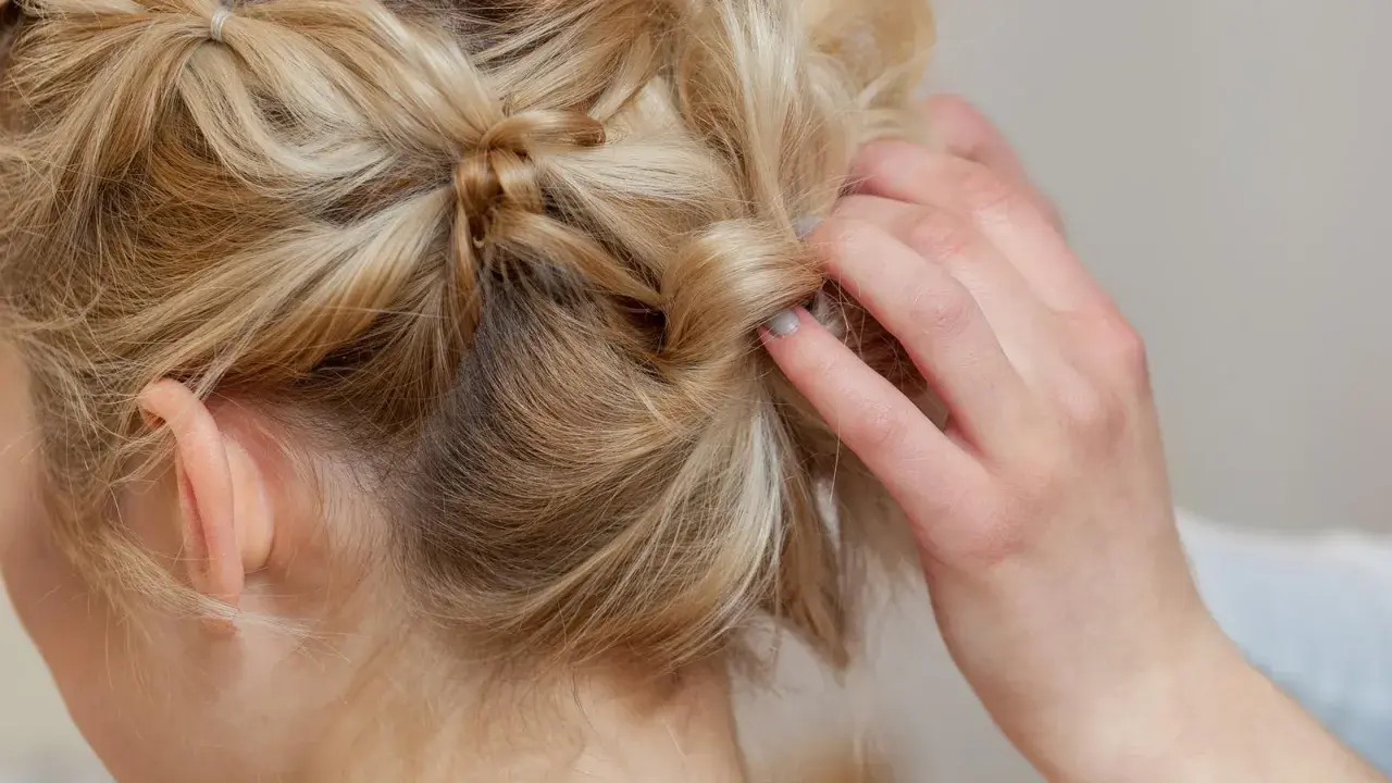 Eine Hand stylt blonde Haare zu verspielten hochsteckfrisuren mittellang. Kleine Zöpfe und gedrehte Strähnen ergeben einen lässigen Look.