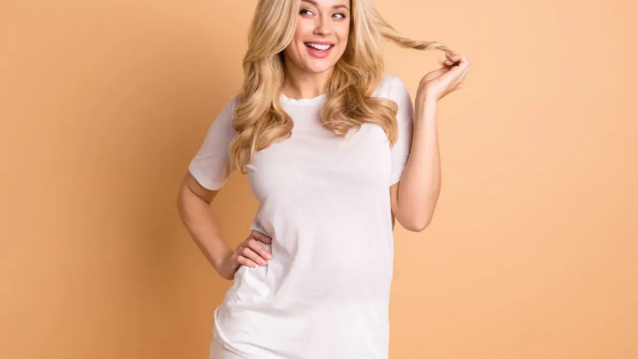 Eine lächelnde Vanilla Girl mit blonden Locken spielt mit einer Haarsträhne. Sie trägt ein weißes T-Shirt und weiße Hose.