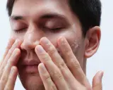 Mann reinigt sein Gesicht mit schäumendem Reinigungsmittel.