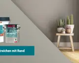 Zwei Eimer Baufix-Farbe, ein großer weißer und ein kleinerer mit "Farbakzente". Daneben ein Hocker mit Pflanzen. Der Slogan "Wand streichen mit Rand" ist zu sehen.