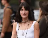 Frau mit mittellangem Haar und Curtain Bangs, trägt ein weißes Tanktop und mehrere Halsketten.