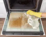 Gelbe Handschuhe reinigen mit Schaum die stark verschmutzte Backofentür.