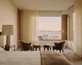 Ein Schlafzimmer mit Blick auf die Stadt und das Meer, gestaltet im Stil einer Feng Shui Wohnung. Sanfte Farben und natürliche Materialien schaffen Harmonie.
