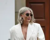 Moderne Frau mit gestuften Frisuren ab 50 mit Brille, trägt cremefarbenen Blazer und auffälligen Schmuck.