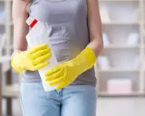 Person in gelben Handschuhen hält Reinigungsmittel. So putzt man Fenster streifenfrei für ein strahlendes Ergebnis.