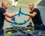 Mann mit blauen Handschuhen putzt mit einem Abzieher den Spiegel.