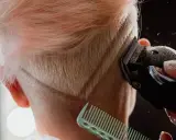 Eine Frau bekommt einen modernen Undercut. Haare werden mit einem Trimmer geschnitten, ein Kamm hält die Strähnen.