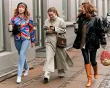 Drei Frauen spazieren mit Kaffee. Die mittlere trägt weite Hosen zu Pumps, die rechte Leggings zu Stiefeln. Die linke zeigt, welche Hose zu Boots Damen passt: Jeans zu weißen Stiefeletten.