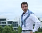 Mann mit klassischer old money hairstyle herren, trägt weißes Hemd und blauen Pullover über den Schultern.