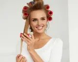 Lächelnde Frau mit roten Wicklern im Haar, die sich Locken macht.