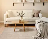 Ein helles Wohnzimmer mit weißem Sofa, Holztisch und Teppich. Perfekt für minimalistisch wohnen.