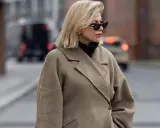 Eine Frau mit blondem Scandi Bob und Sonnenbrille trägt einen beigen Wollmantel und schwarzen Rollkragenpullover.