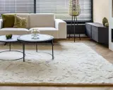 Ein heller, flauschiger Teppich liegt vor einem Sofa und einem Kamin. So wird der Teppich wieder flauschig gemacht.