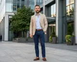 Ein Mann in einem hellbeigen Sakko und hellblauem Hemd, dazu dunkelblaue Hose. Ein klassischer Look, der immer passt.