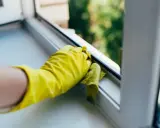 Gelbe Handschuhe reinigen den Kunststoff Fensterrahmen mit einem Tuch.