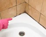 Mit rosa Handschuh wird auf stark verschmutzte Dusche reinigen hingewiesen. Schimmel und Dreck in den Fugen.