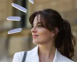 Frau mit rundem Gesicht und Curtain Bangs, trägt weißen Blazer.