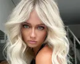 Blonde Frau mit voluminöser blowout frisur und blauen Augen blickt ernst in die Kamera.
