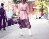 Ein Midirock kombiniert mit einem rosa Pullover und weißen Stiefeln – ein lässiger Sommer-Look auf der Straße.