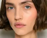 Nahaufnahme einer Frau mit einem kurzen Bob-Haarschnitt, blauen Augen und rosafarbenen Wangen.